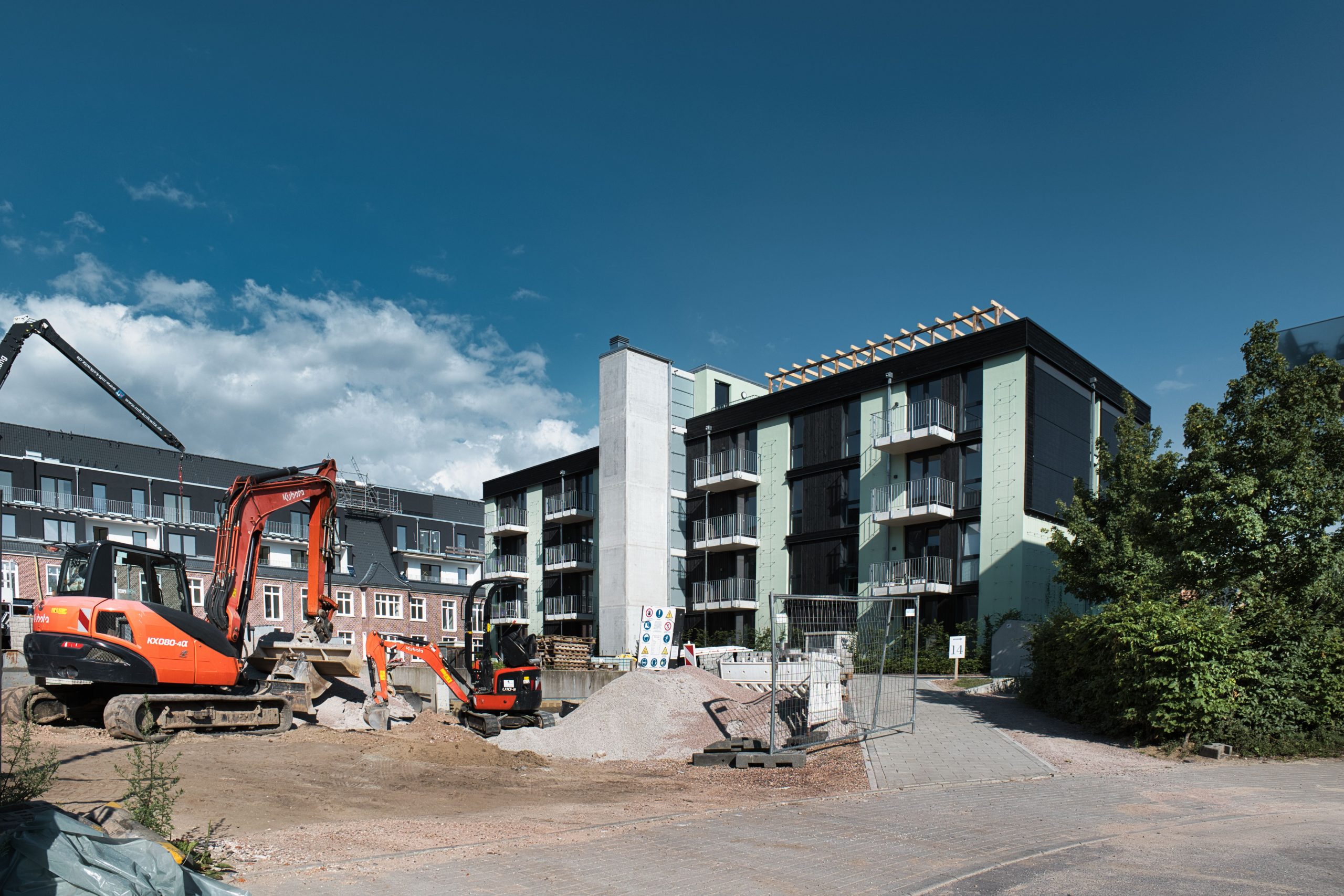 Active construction site with machinery next to modern apartments under blue sky.